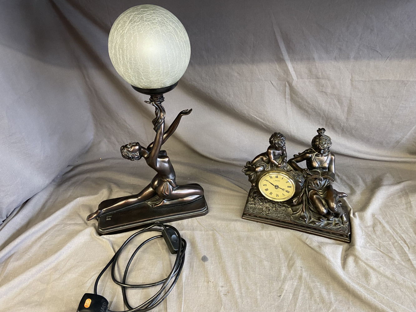 2 statues one with a clock and the other art deco style lamp
