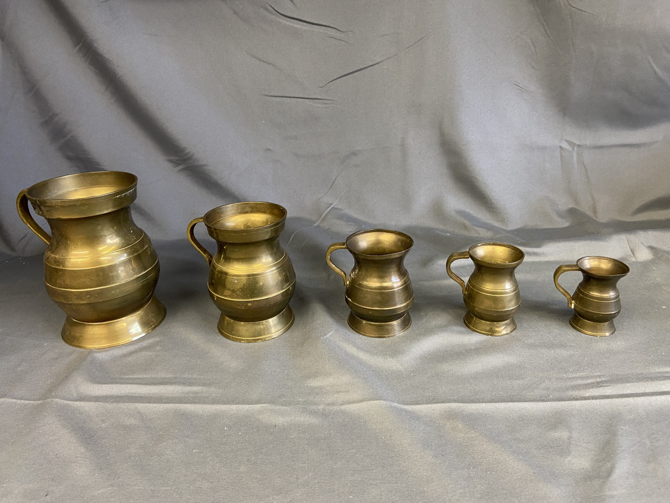Graduating brass measuring cups, tallest one is 13cms