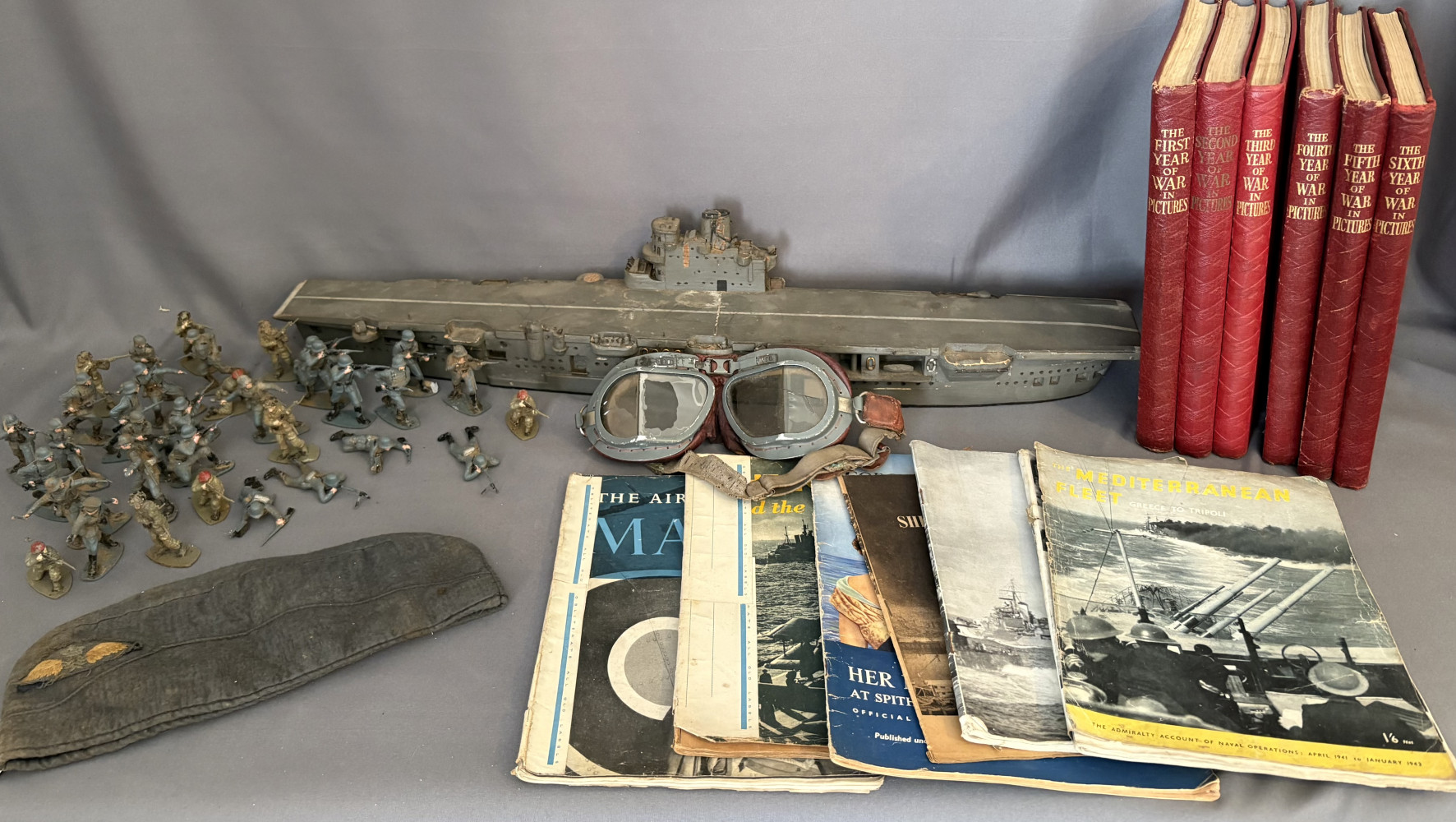 World War II era German Luftwaffe overseas side cap, plastic toy soldiers, aircraft carrier model, antique flying goggles crack lens and selection of war and boat books