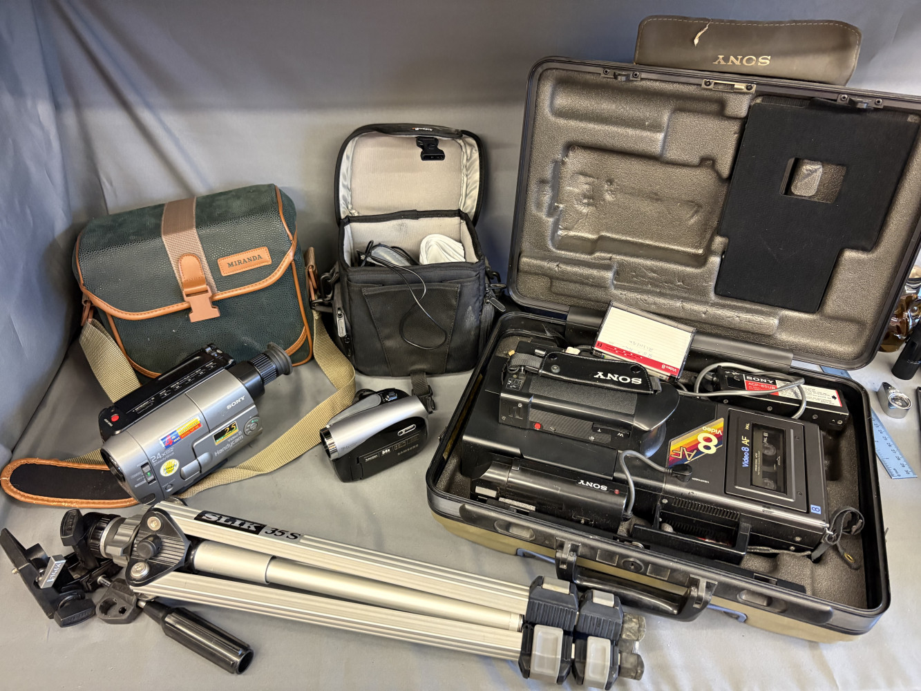Three video cameras one compact silver and black Samsung VP-DX100, Sony CCD-V8AF 8mm Video 8 Video Camera Recorder and Hard Case and a Sony Handycam Vision (CCD-TRV21E PAL) all in cases and a camera tripod