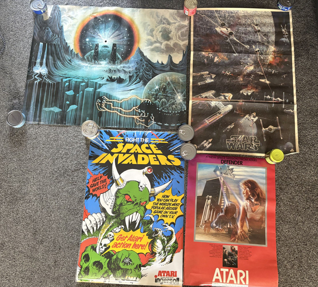 Four vintage posters, vintage promotional poster for the Atari 2600 game Defender, laminated space invaders, vintage 1977 Star Wars "Death Star Battle" promotional poster and  vintage 1990s fantasy art poster titled "Genesis"