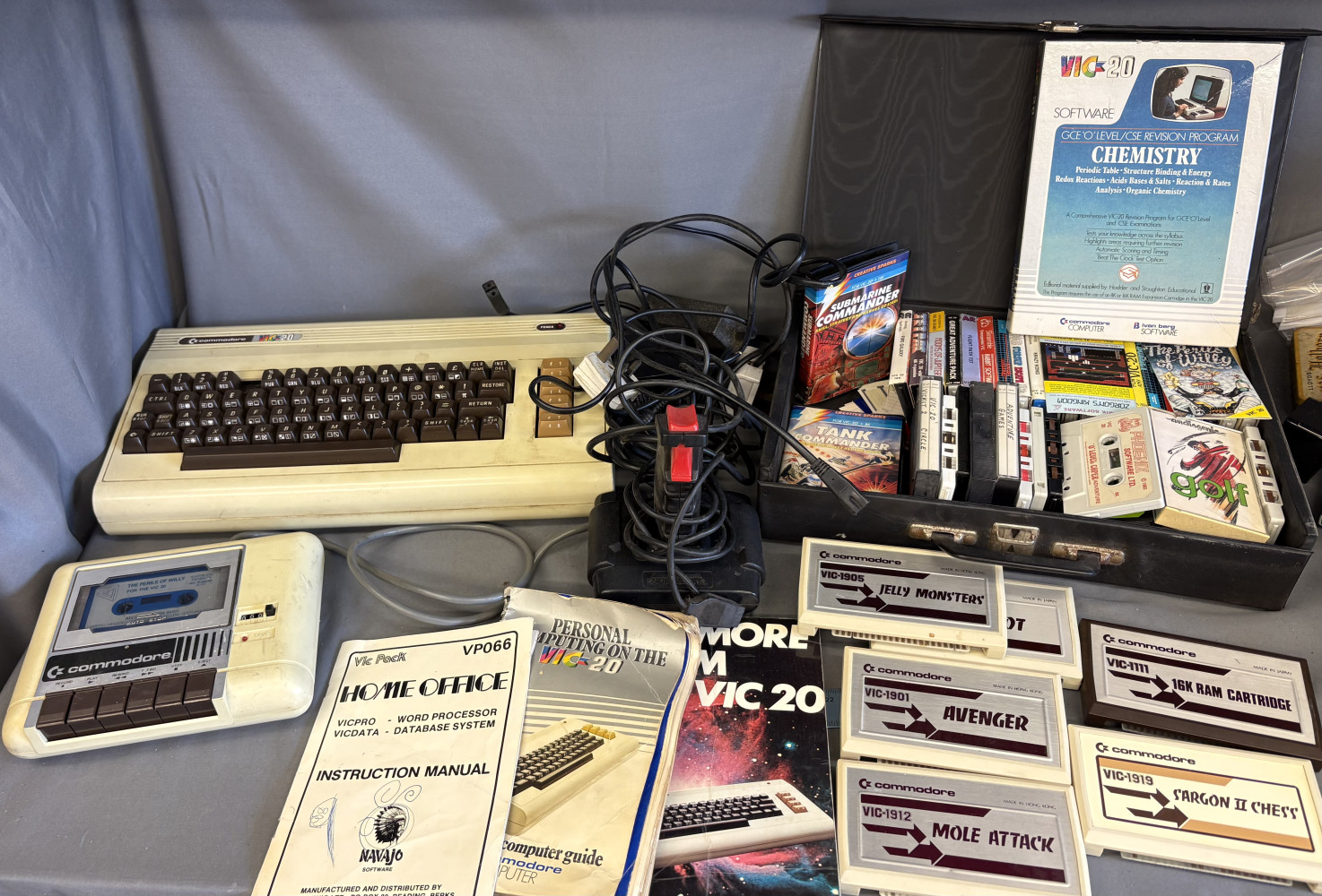 Vintage Commodore VIC-20 home computer system with a cassette datasette, joystick, manuals, and several game cartridges and cassettes