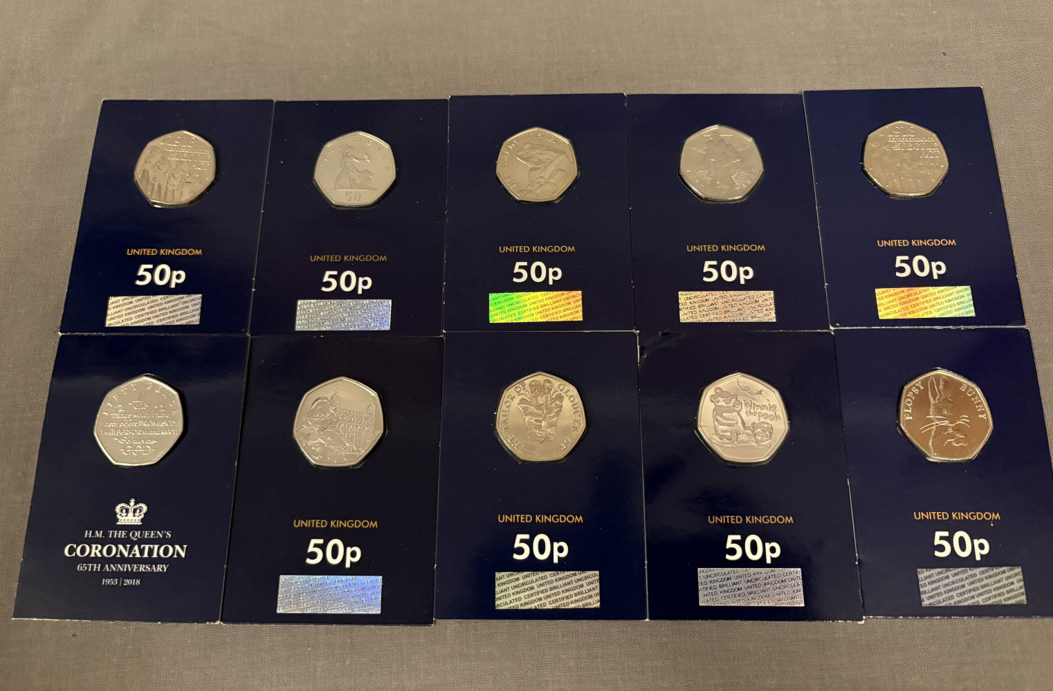 10 collectable 50ps, including 150th Anniversary of the Institution of the Victoria Cross, Winnie the Pooh, Paddington bear, Flopsy Bunny, Coronation Oath, Mr. Jeremy Fisher, 2 x Representation of the People Act, Britannia and a The Tailor of Gloucester